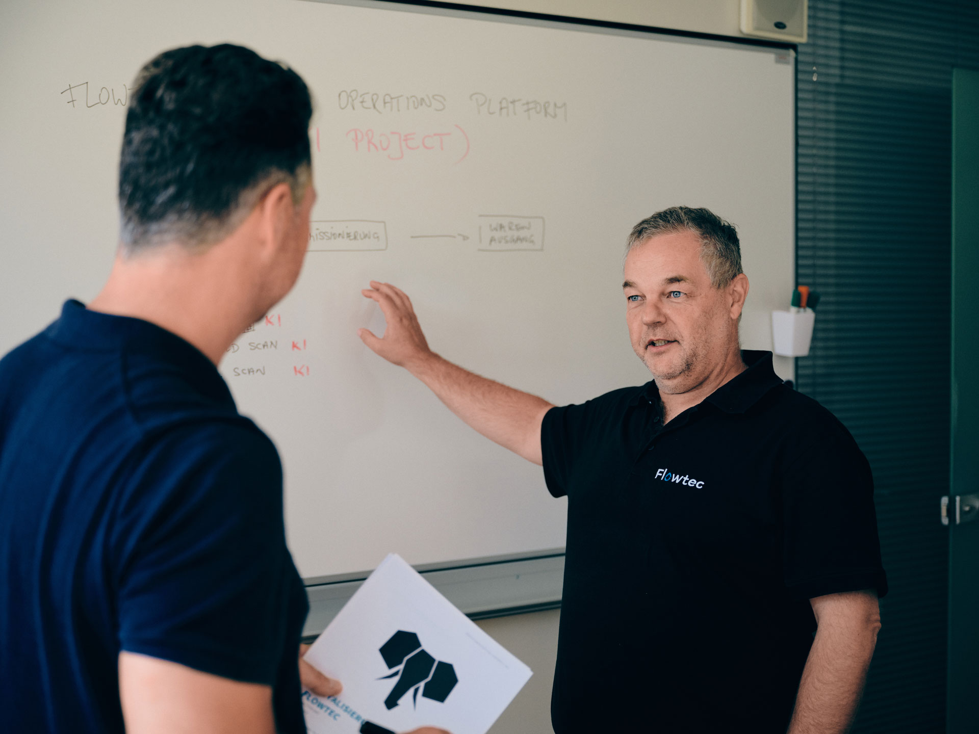 Zwei Flowtec-Mitarbeiter im fachlichen Austausch an einer Whiteboard-Tafel